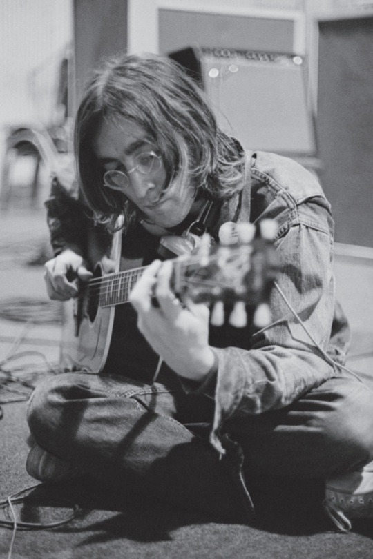 Black and white photo of John Lennon playing a guitar.